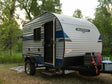 A Sunray Sport travel trailer rv rental in a scenic campsite, featuring an open door, generator, and propane tank.