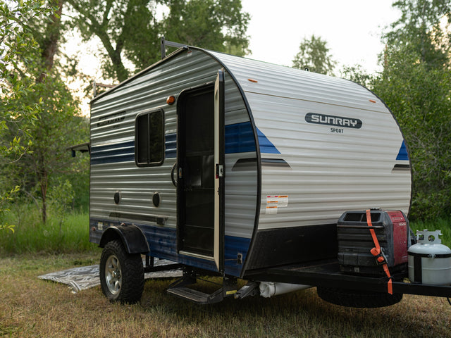 A Sunray Sport travel trailer rv rental in a scenic campsite, featuring an open door, generator, and propane tank.