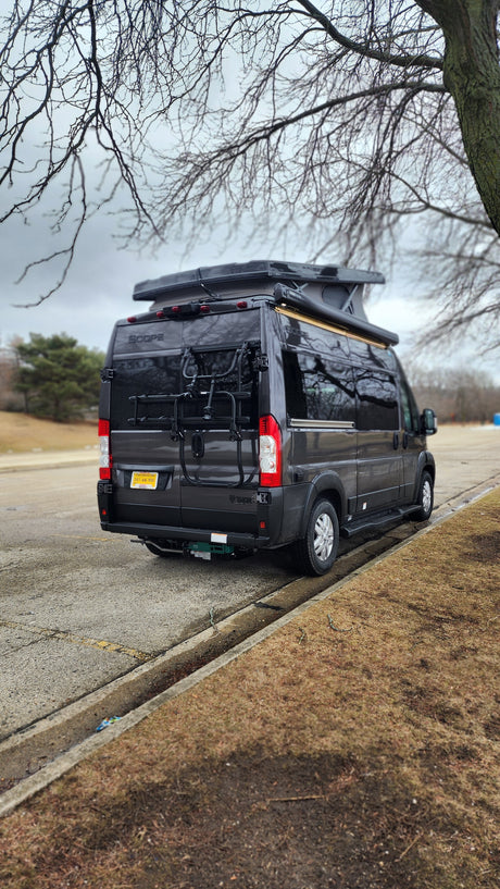A dark gray Winnebago Scope Class B camper van, an RV rental, parked roadside. Features a pop-top roof & rear bike rack.