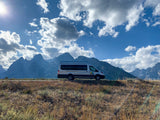 Silver WanderVans RV rental camper van overlooking majestic mountains under a bright, cloudy sky. Perfect for outdoor travel.
