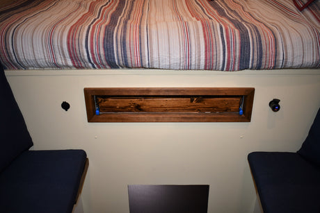 RV rental interior: striped bed, wood storage, USB charge port, & comfy seating.