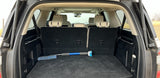 Inside a large SUV's trunk: folded third-row seats reveal vast cargo space. A cleaning tool rests. Ideal for RV rental trips or adventure.
