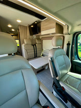 Explore the modern interior of this RV rental, showcasing comfortable leather seating, a functional dining area, and TV.