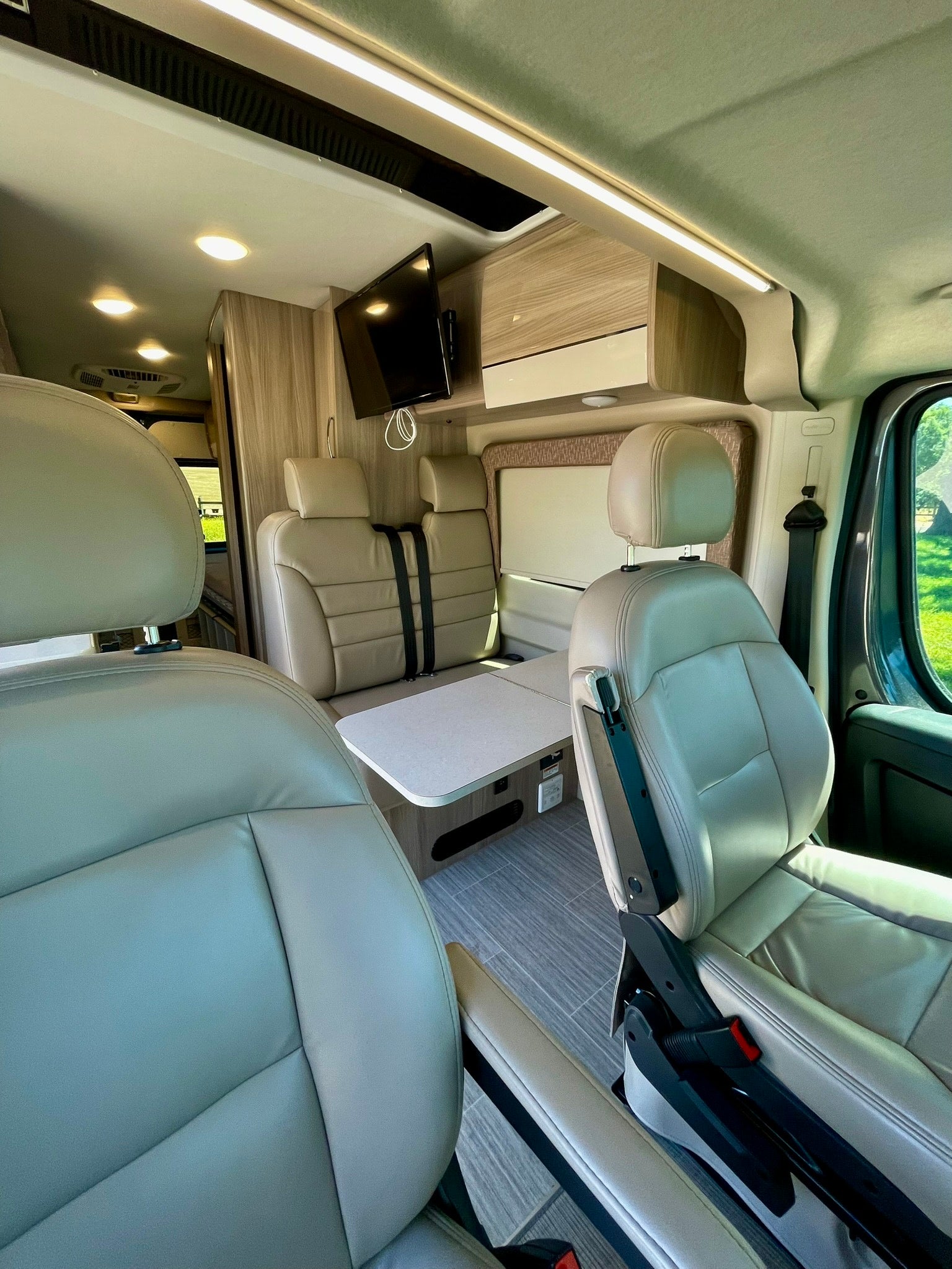Explore the modern interior of this RV rental, showcasing comfortable leather seating, a functional dining area, and TV.
