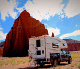 An RV rental truck camper is parked before majestic red rock formations under a blue sky, perfect for desert exploration.