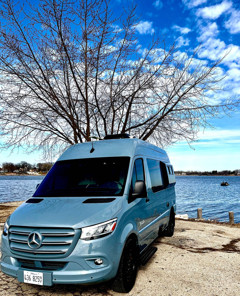  with a bare tree and fishing boat.|RV rental on the beach: Enjoy cooking & stunning ocean views from this van's modern kitchen & comfy seats.|Inside an RV rental: quilted bed — photo 9