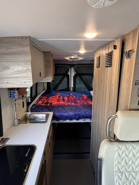 Cozy RV rental interior with a kitchenette, overhead storage, and a bed, ready for your next road trip adventure.