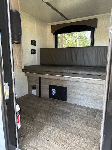 RV rental interior with compact bench seating, window view, wall-mounted control panel, speaker, and fire extinguisher.