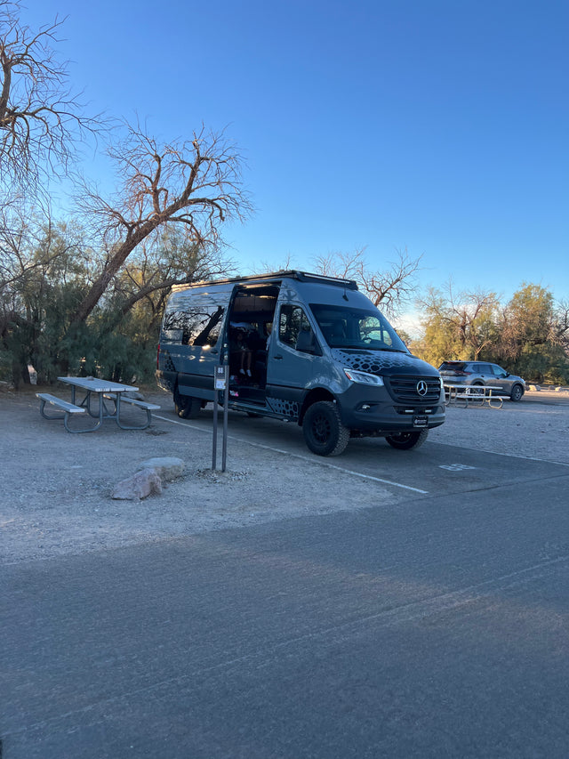 Grey Mercedes Sprinter camper van at campsite 88 with an open door, ready for an RV rental trip. A picnic table is nearby.