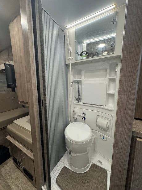 Compact RV rental bathroom features a toilet, sink/shower combo, and mirror, maximizing space for travel comfort.