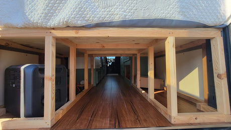 Inside an rv rental, showing a custom wood bed frame, under-bed storage for gear like a portable power station.