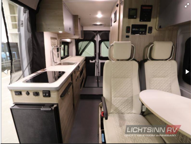 Inside an RV rental: a compact camper van with a kitchenette, cream swivel seats, and control panels.