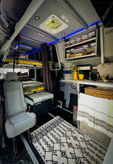 Spacious rv rental interior: bunk beds, compact kitchen, Dometic fridge, and overhead storage under blue light.