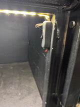 Bright LED strip lighting illuminates this RV rental storage compartment, featuring an accessible control switch on the wall.