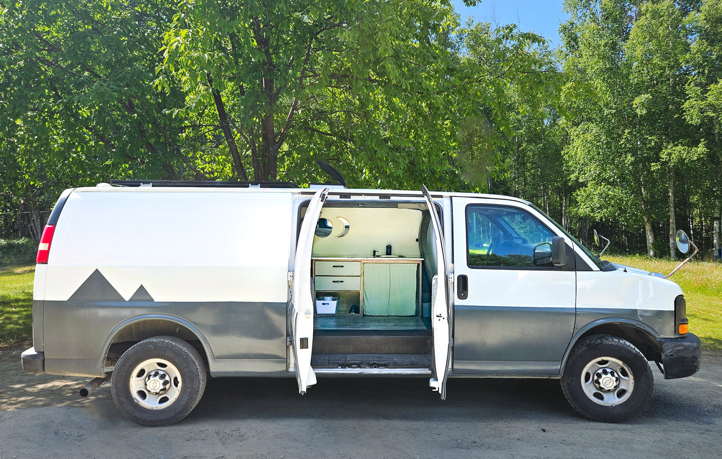 A custom white and gray camper van with mountain decals, its side door open to reveal a built-in kitchen. Ideal for RV rental.