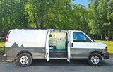 A custom white and gray camper van with mountain decals, its side door open to reveal a built-in kitchen. Ideal for RV rental.