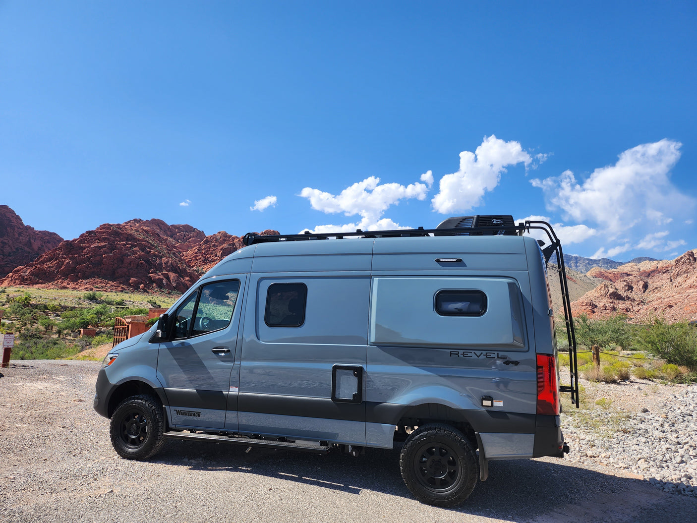 Adventure-ready Winnebago Revel 4x4 RV rental parked in scenic red rock mountains under a clear sky.