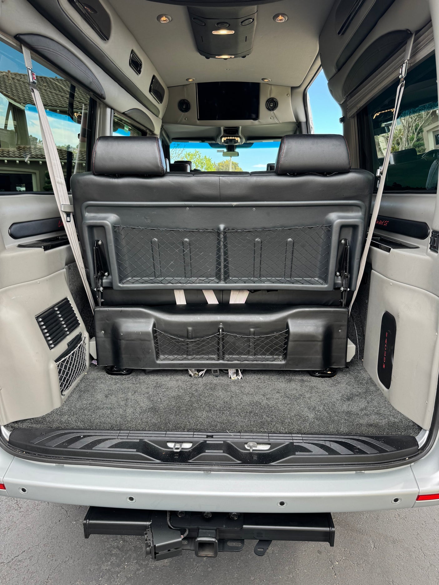 RV rental: View from the rear cargo area showing folded seats with storage nets, carpeted floor, and overhead entertainment system.