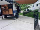A white teardrop RV rental camper with an open outdoor kitchen is parked on a driveway. Ready for adventures.