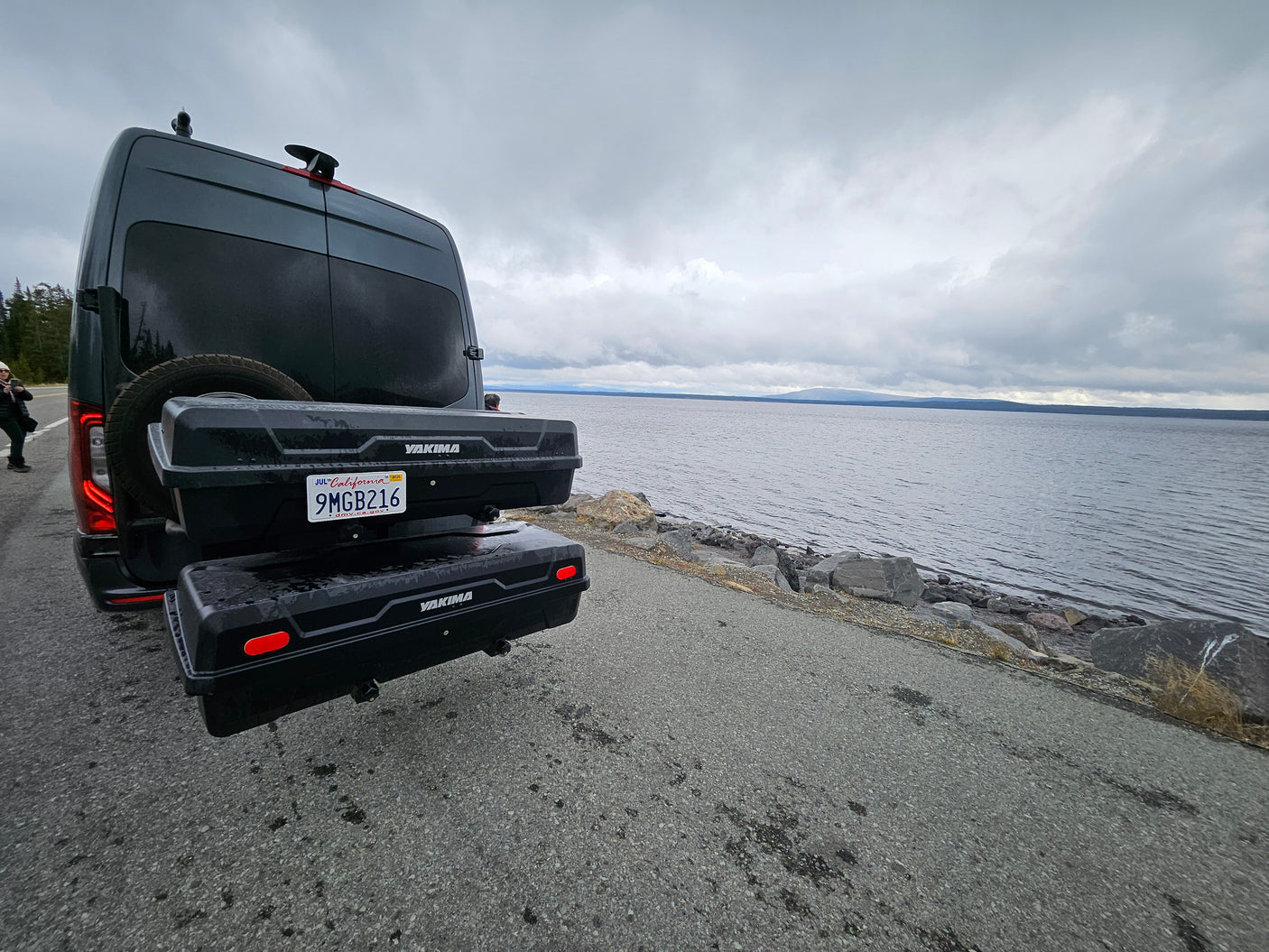 Explore by water! This RV rental camper van, equipped with Yakima cargo boxes, is perfectly parked beside a serene, overcast lake.