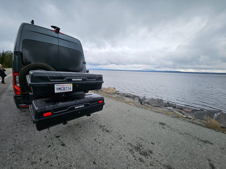 Explore by water! This RV rental camper van, equipped with Yakima cargo boxes, is perfectly parked beside a serene, overcast lake.