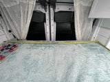 Cozy RV rental sleeping area: Bed with measuring tape, sheer curtains frame rear van doors.
