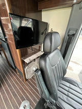 Cozy rv rental interior featuring a padded black seat with armrests, flat-screen TV, and striped wood-look flooring. Ready for your journey.