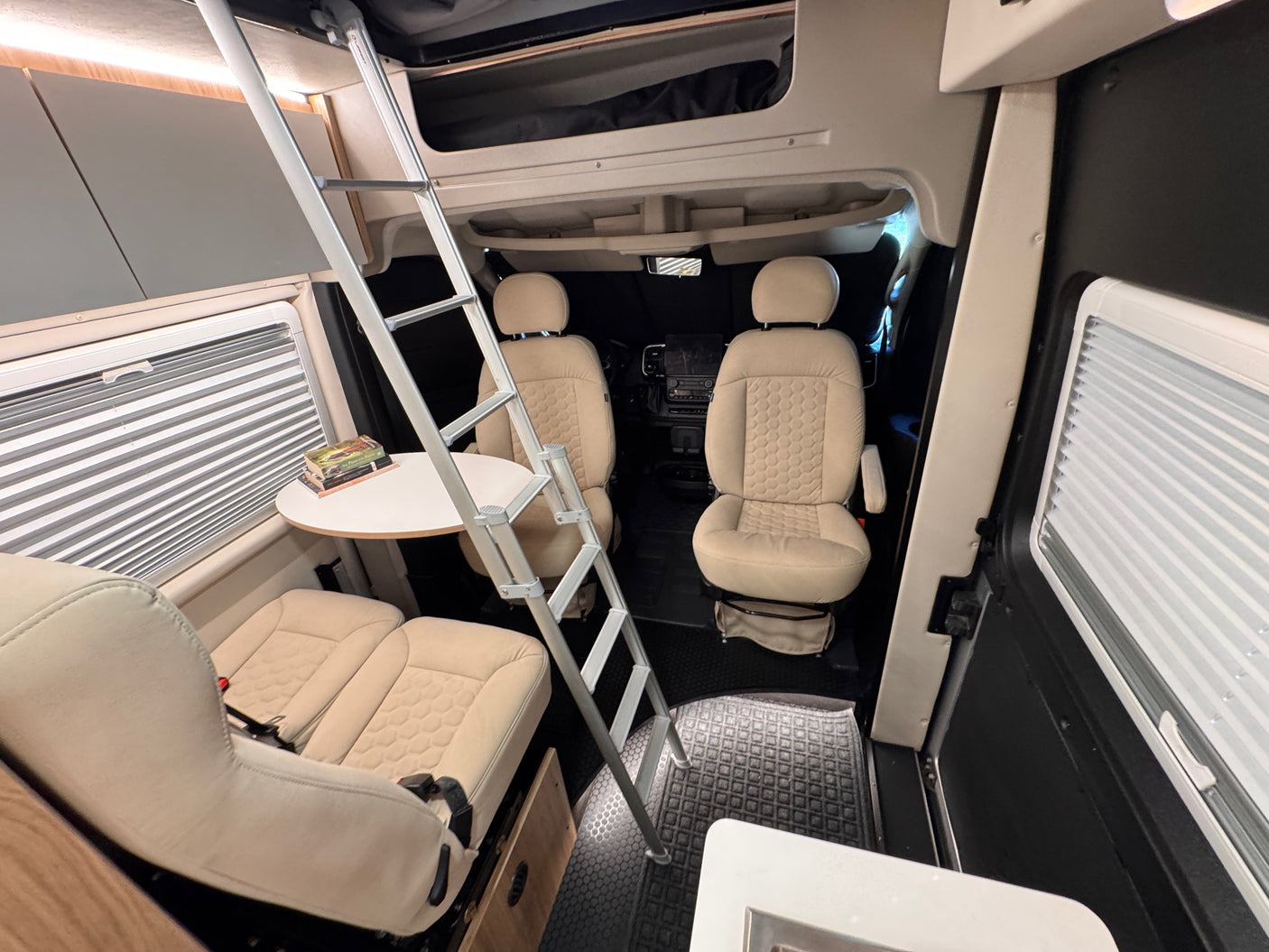 Cozy RV rental interior with swivel captain's chairs, dining table, and a ladder to an overhead sleeping area.
