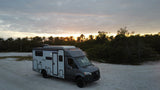 RV rental: A grey Mercedes-Benz camper van parked on sandy terrain at sunrise/sunset, with a warm sky glow.