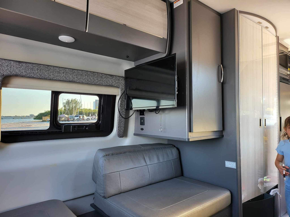 Cozy RV rental interior with bench seating, TV, overhead cabinets, and a window view of the beach. — photo 14