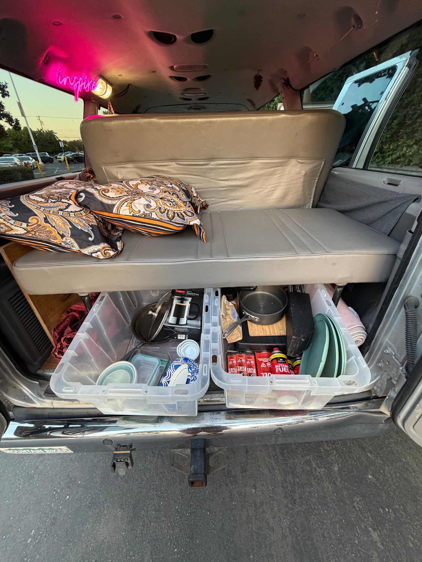 Inside an rv rental: a cozy camping setup with kitchen essentials in pull-out bins (French press, pots, butane) and a bench seat. An "inspire" sign glows.