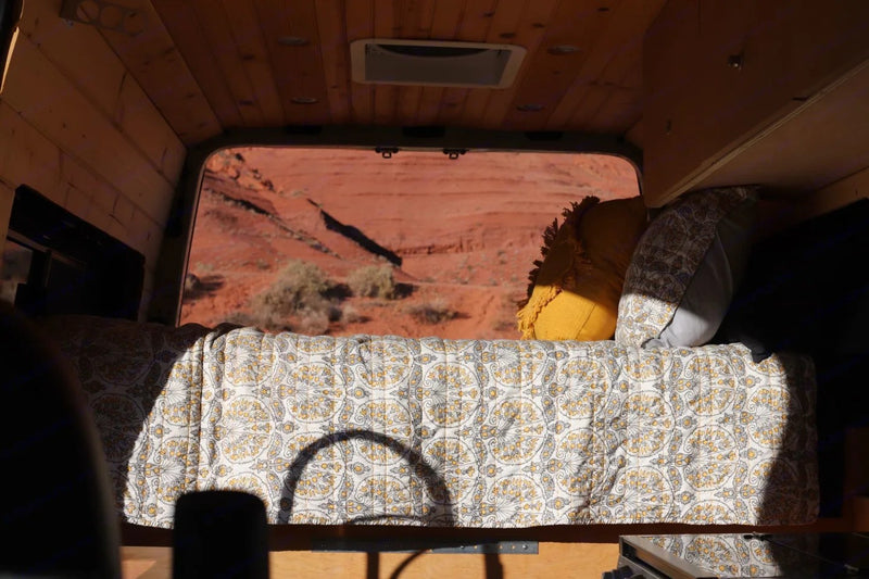Cozy camper van bed inside an RV rental, offering a panoramic view of a red desert landscape through the back window. — photo 5