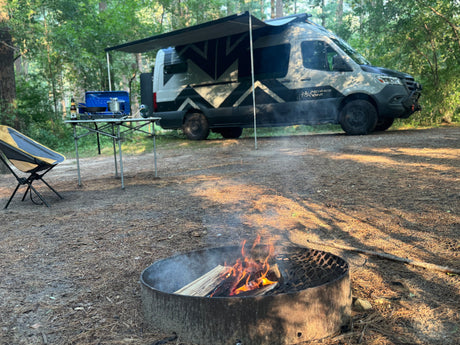 A perfect RV rental campsite: campfire, outdoor cooking, and a modern camper van with awning. Ideal for outdoor adventures.