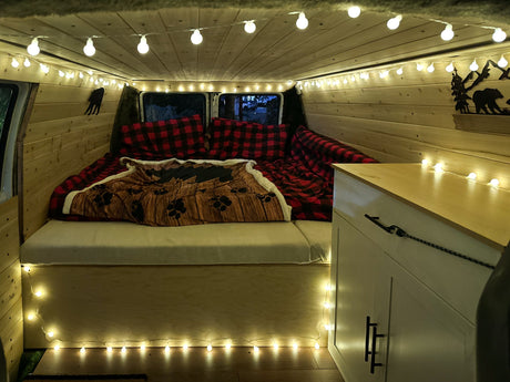 Cozy camper van interior, perfect for an RV rental. Features wood walls, string lights, and a plaid-covered bed.