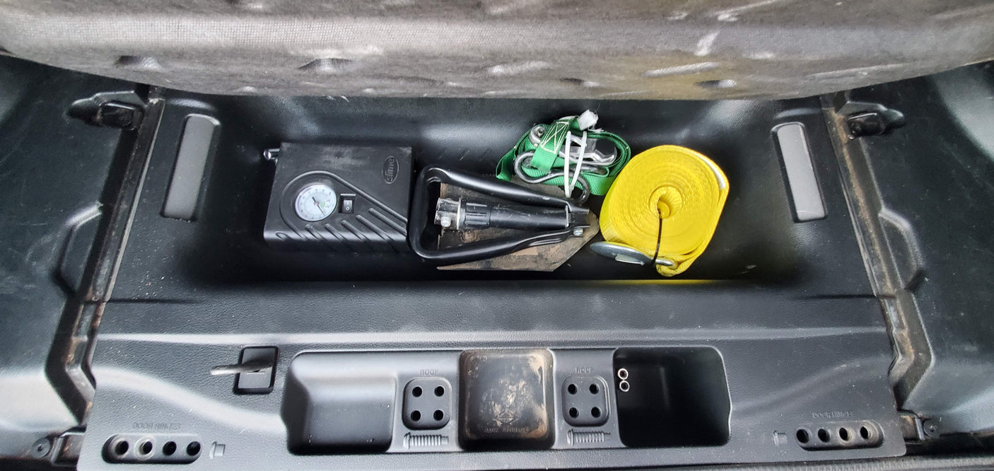 RV rental storage shows air compressor, yellow recovery strap, green tow straps, and jack tools for emergencies.