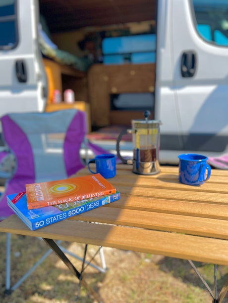 Morning coffee & travel books outside an RV rental. A French press, mugs, and "50 States 5000 Ideas" await.