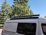Grey RV rental van with a black CVC roof awning, parked outdoors under clear skies.