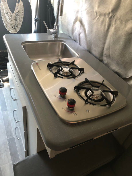Compact rv rental kitchen: built-in sink with faucet & two-burner Suburban stove. Ideal for on-the-go cooking.