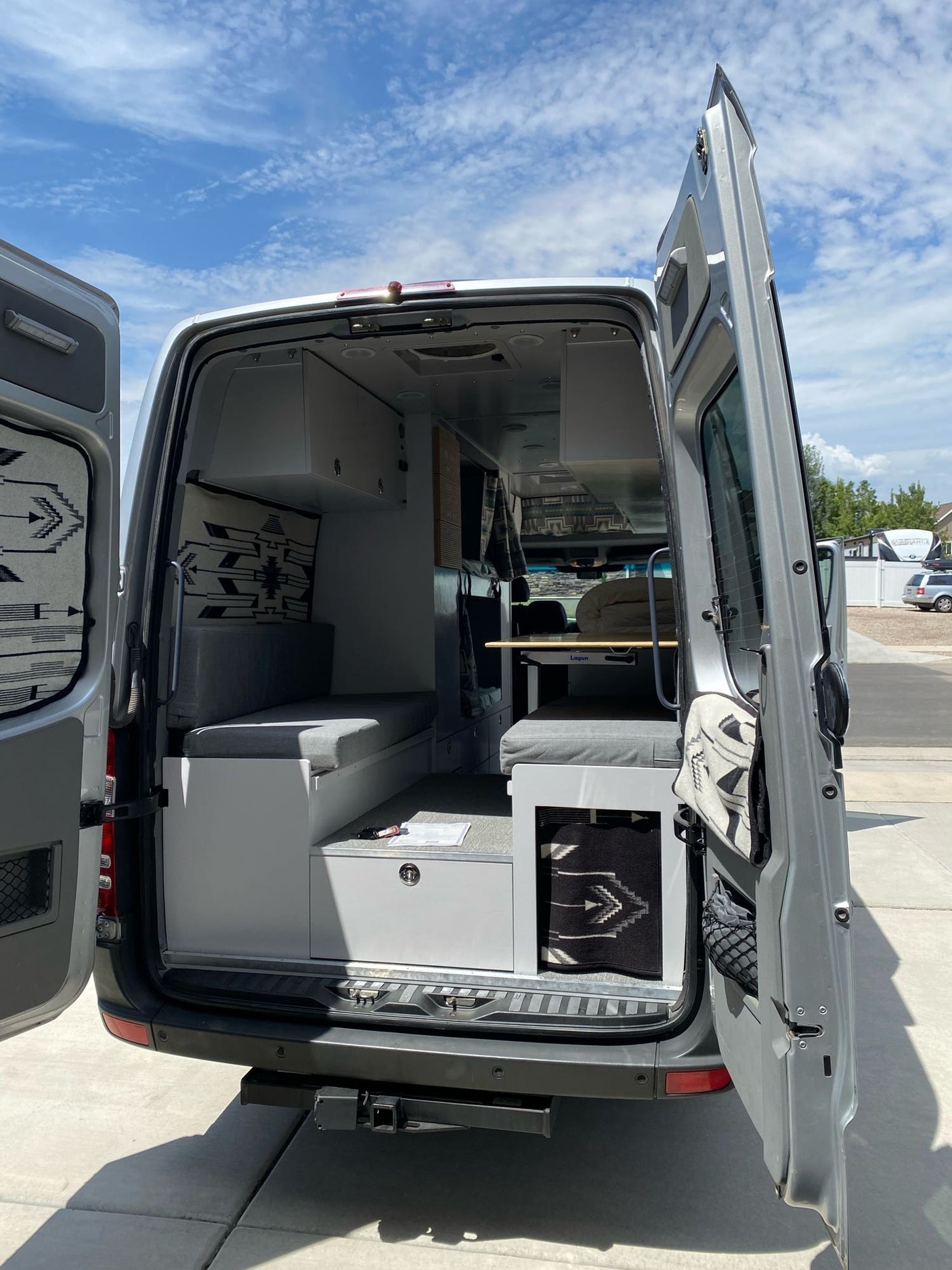 Rear view of a modern RV rental camper van with open doors, revealing its organized interior: seating, table, storage.