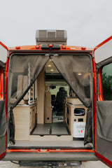 RV rental with open rear doors, revealing a cozy wood interior, mesh screen, and roof AC unit.