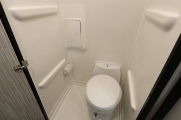 See inside an RV rental! This compact, all-white RV bathroom features a toilet, toilet paper holder, and wall-mounted cabinet.