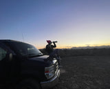 Relaxing on an RV rental van at desert sunset. Person drinks from bottle; mountains in view.