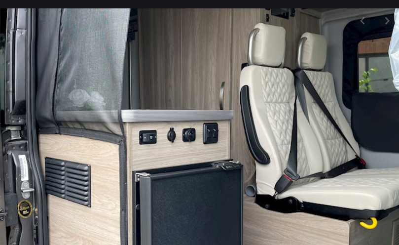 Modern RV rental interior: integrated fridge, power outlets, and plush passenger seating for your journey.