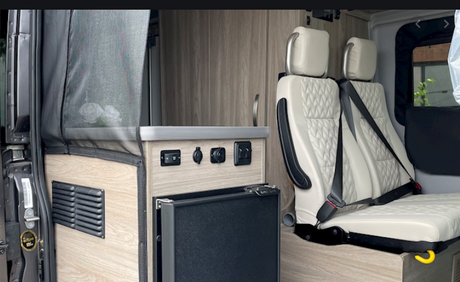 Modern RV rental interior: integrated fridge, power outlets, and plush passenger seating for your journey.