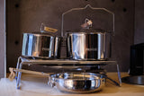 Shiny Primus camping pots and pan on a portable burner stand. Essential cookware for an RV rental outdoor cooking.