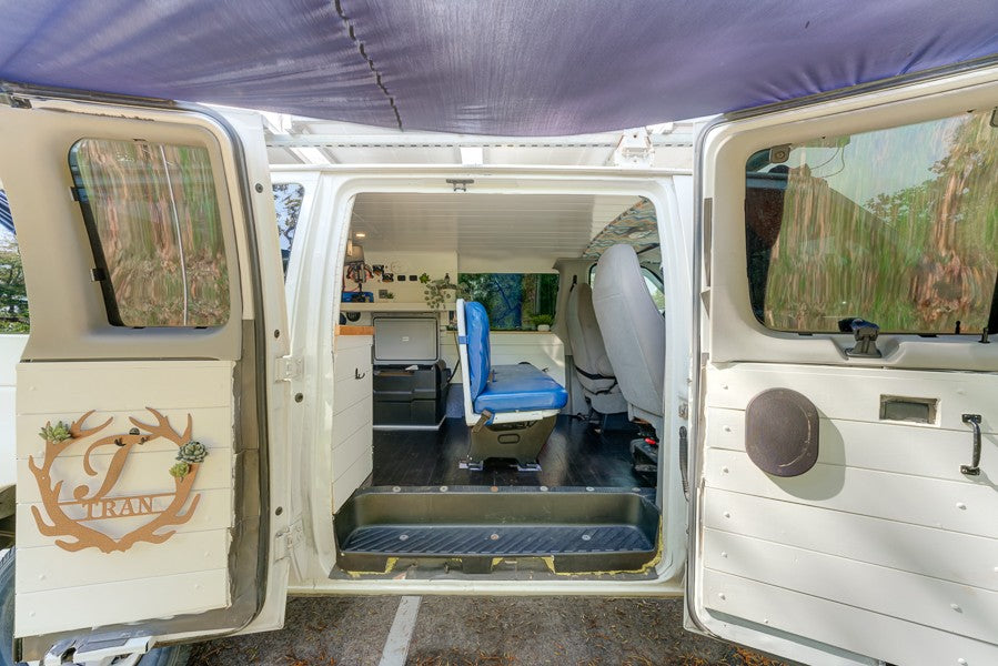 Inside this custom RV rental van conversion: a cozy interior with a blue seat, storage, and personalized decor.