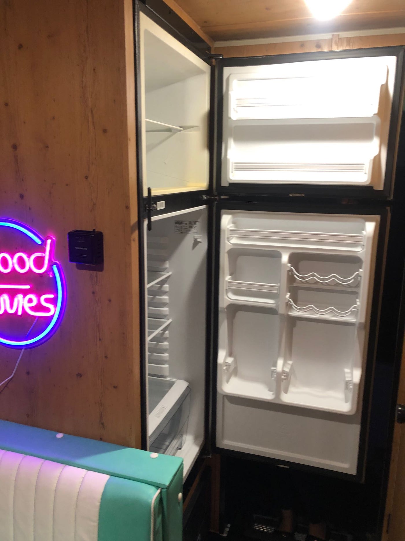 RV rental interior features an open, empty compact refrigerator-freezer, neon 'good vibes' sign, and striped bench. — photo 16