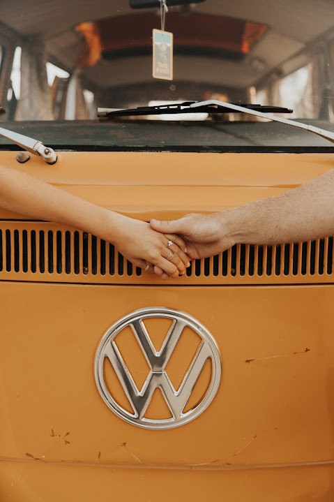 A couple's hands connect over the grille of a vibrant orange vintage VW camper van, ideal for a memorable RV rental adventure. — photo 2