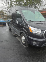 Black high-roof van, suitable for RV rental, parked on wet pavement with side steps and rain droplets.