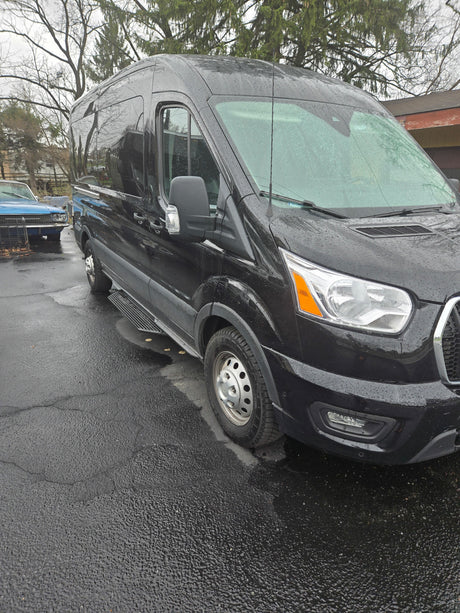 Black high-roof van, suitable for RV rental, parked on wet pavement with side steps and rain droplets.